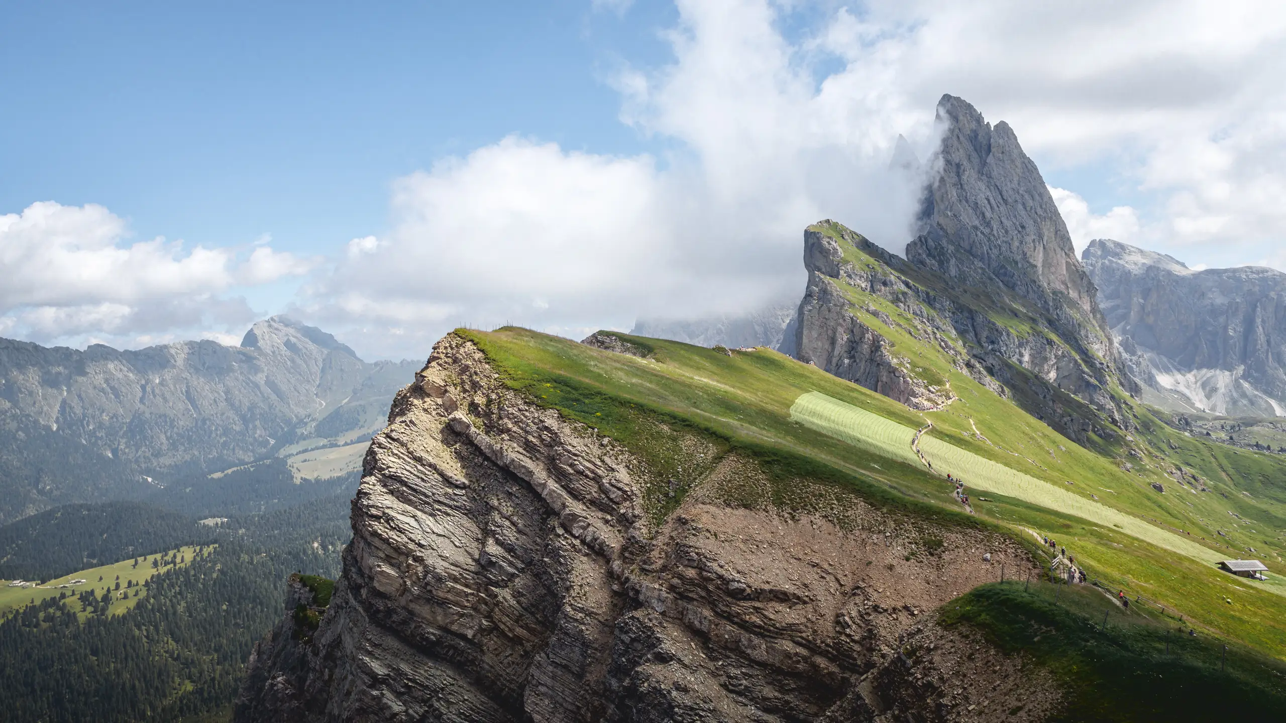A steep grass-topped ridge falling away below jagged peaks, cloud catching the summits