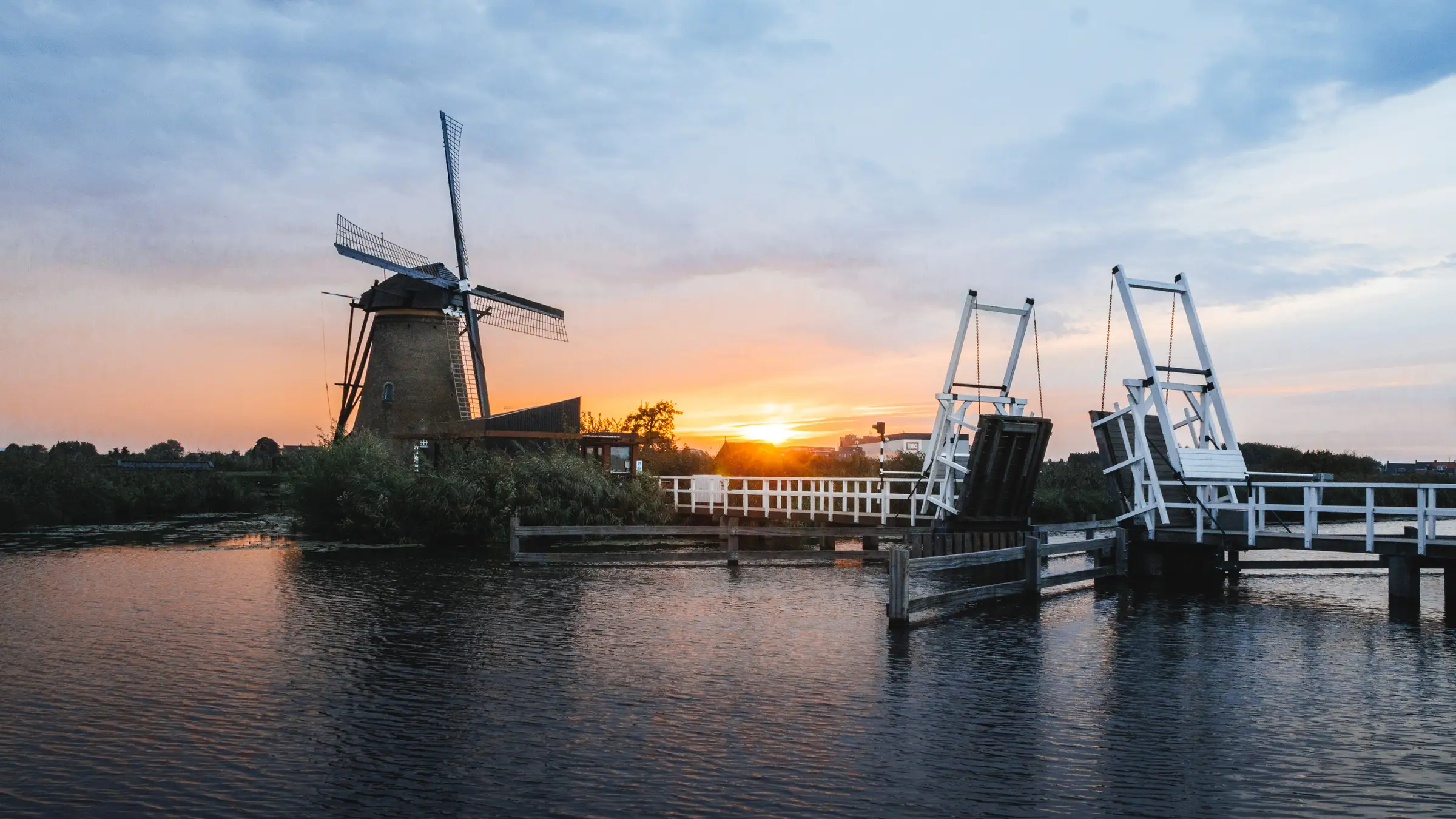 A windmill and a raised white drawbridge over still water at sunset