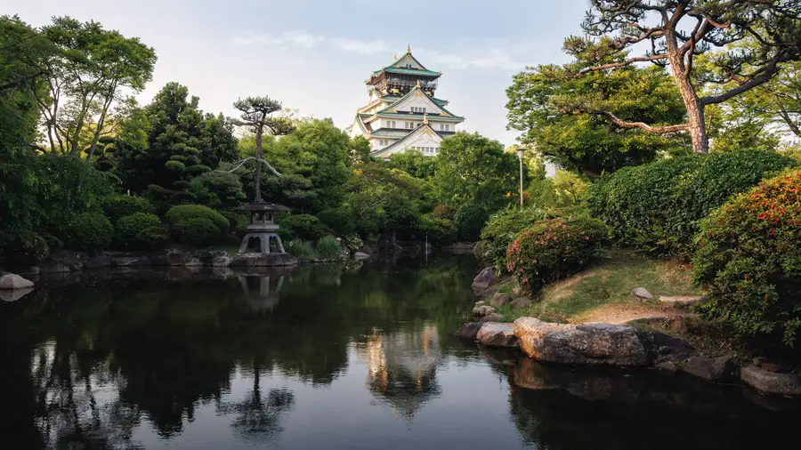 A castle keep above a garden pond with a stone lantern in the foreground