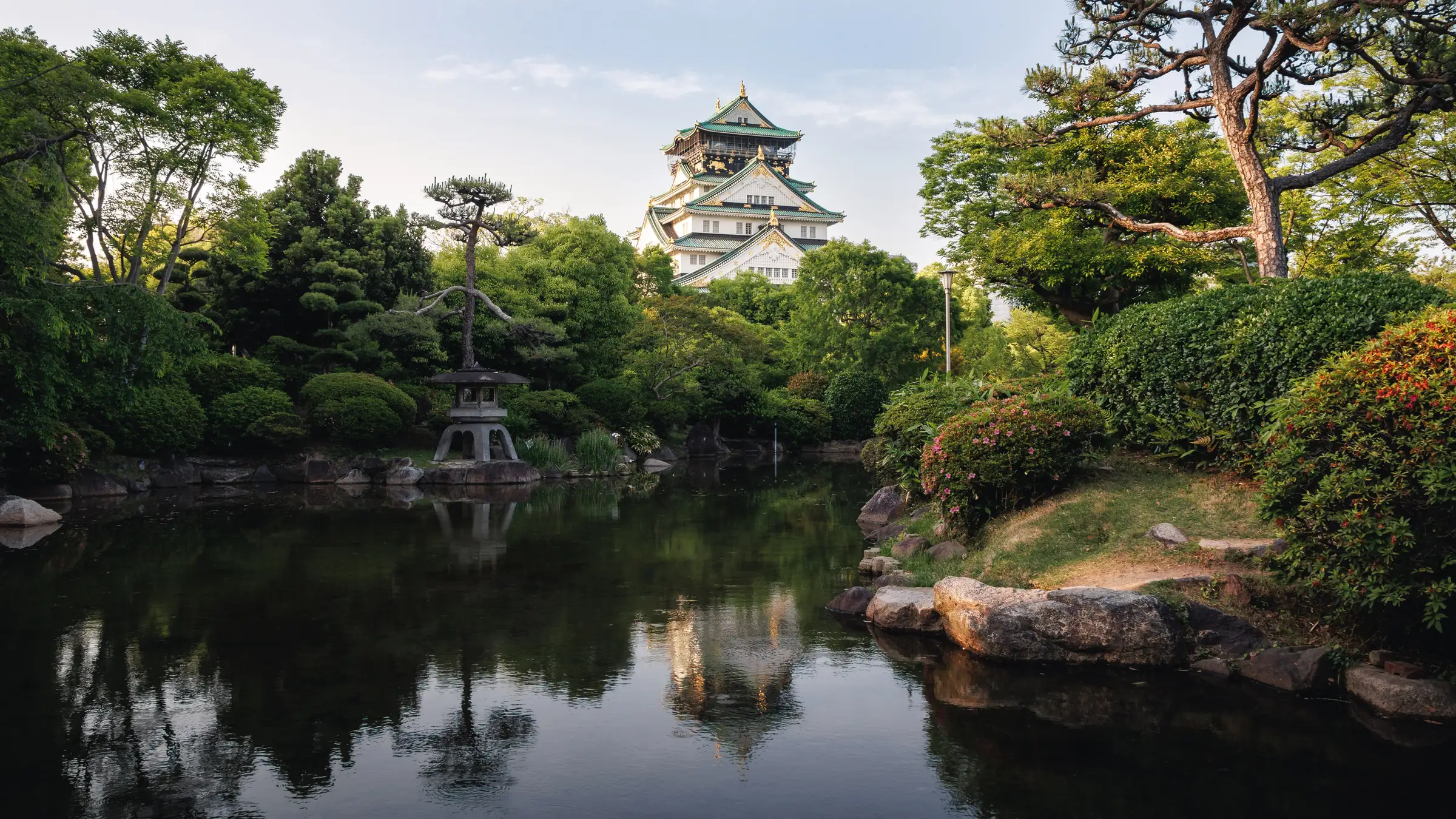 A castle keep above a garden pond with a stone lantern in the foreground