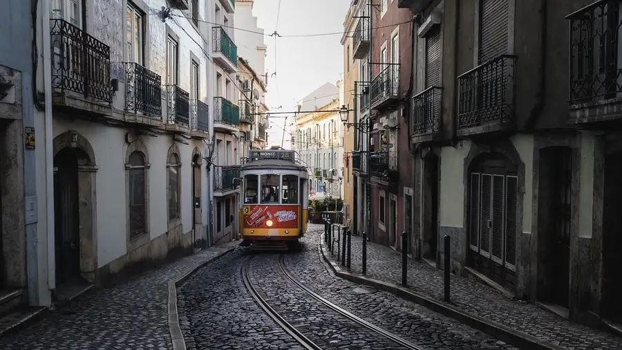 A yellow tram coming up a narrow cobbled street between tiled facades