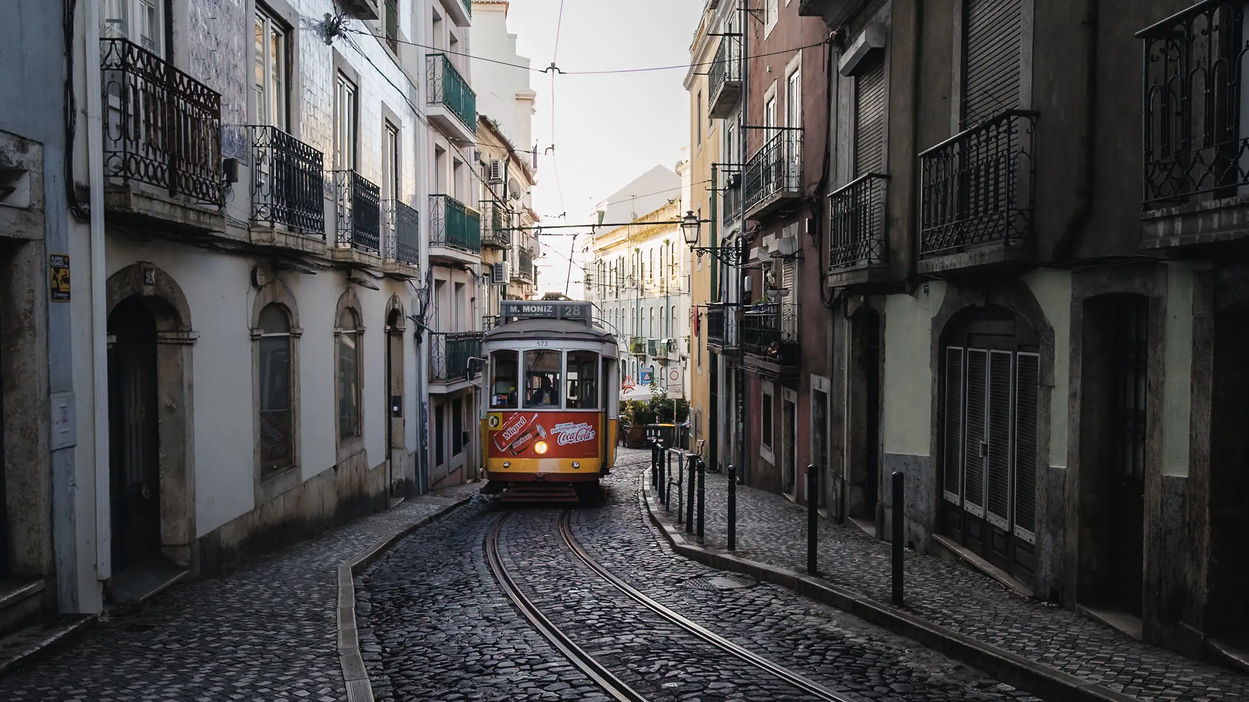 A yellow tram coming up a narrow cobbled street between tiled facades
